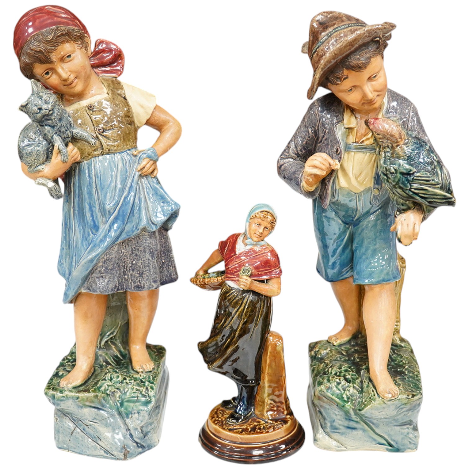 A pair of Austrian majolica figures of children, one holding a cat, the other a parrot, together with a similar smaller figure, tallest 37.5cm high (3). Condition - fair